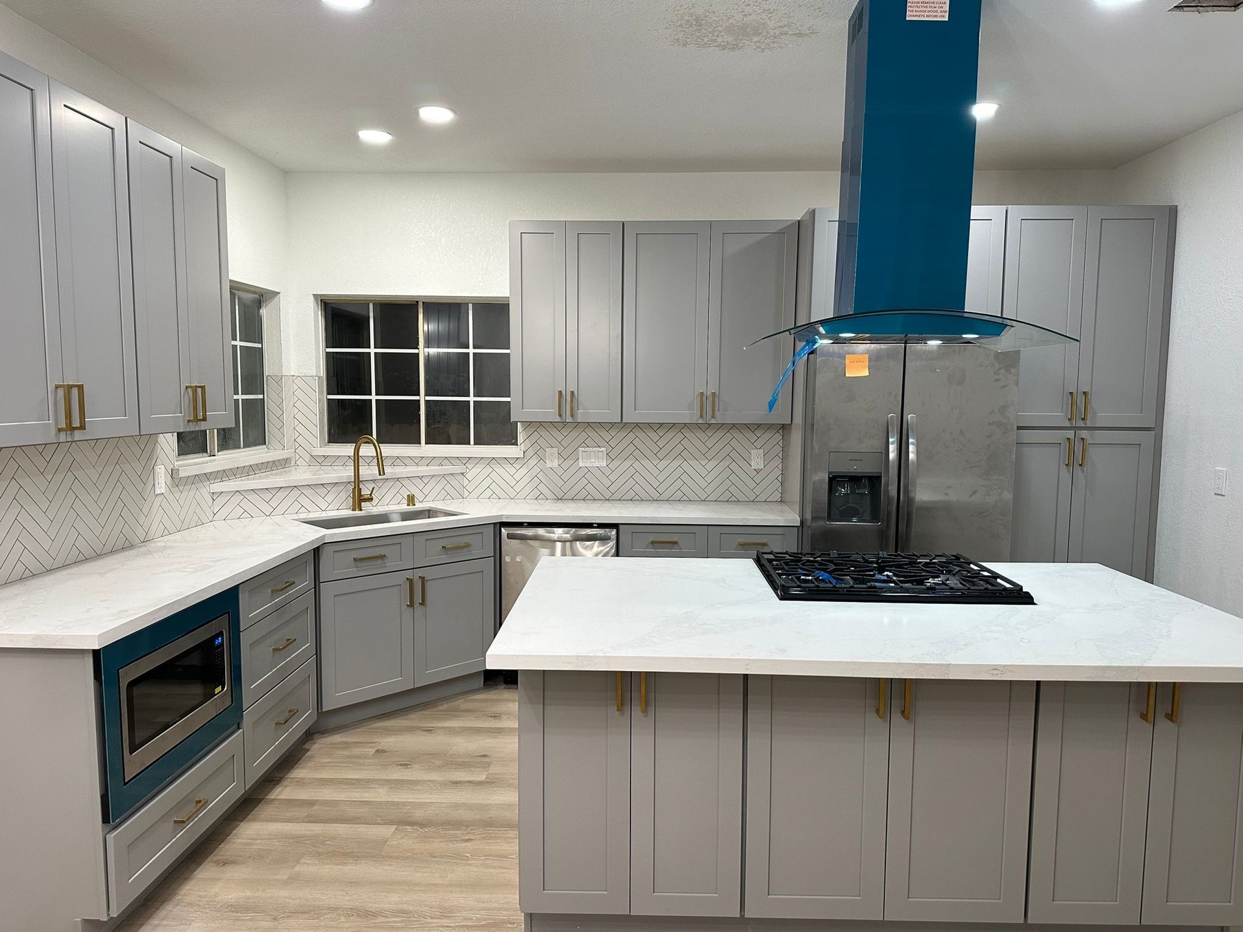Finished white kitchen remodel with large island, gas cooktop, and blue range hood