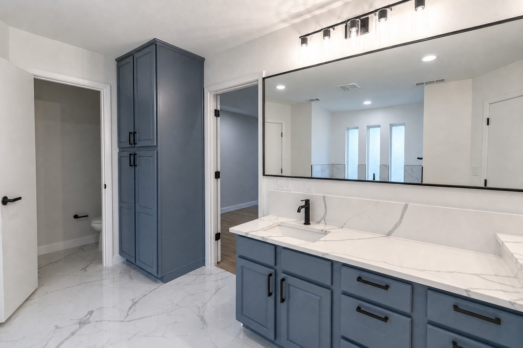 Master bath vanity with blue gray cabinetry, linen storage, and marble-look tile
