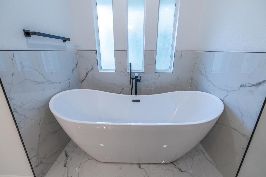 Freestanding tub with marble-look tile surround and tall privacy windows