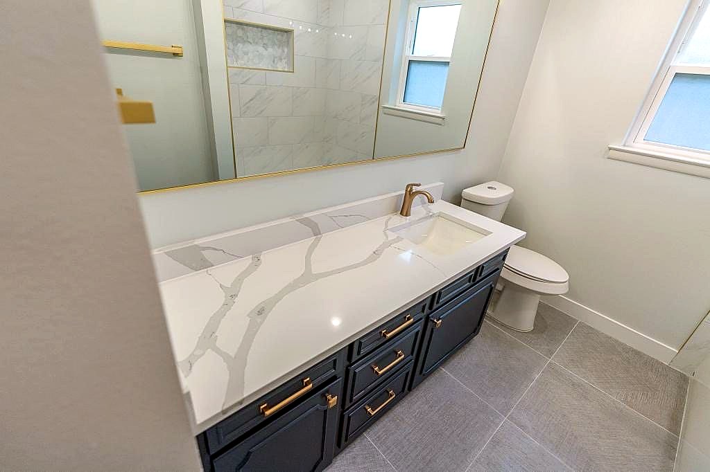 White and gold bathroom with blue vanity, brass accents, and marble-look finishes