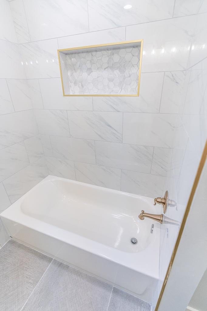 Tub and shower wall with brass fixtures and marble-look tile niche