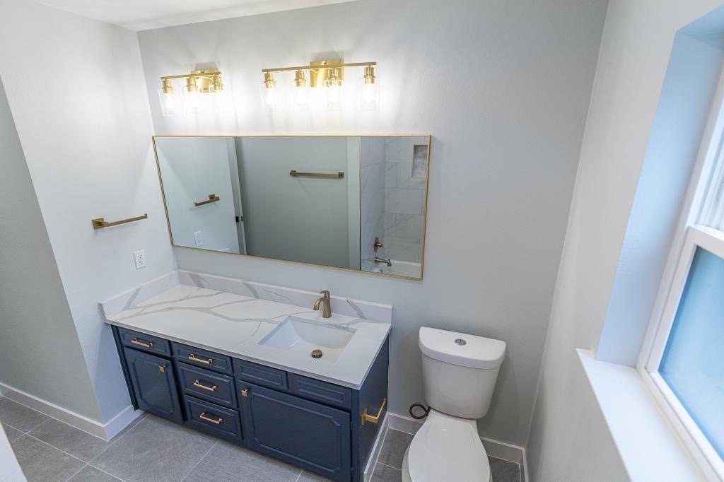 Finished bathroom vanity wall with brass lighting, mirror, and blue cabinetry