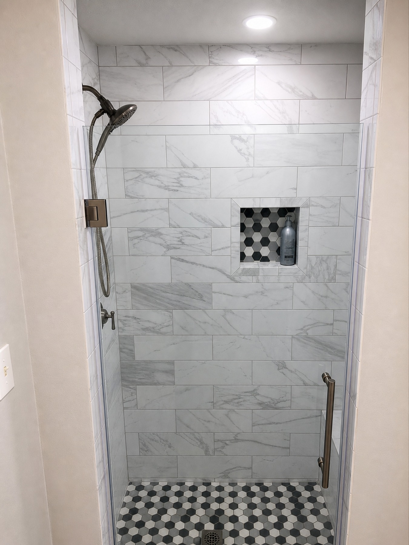 Glass shower with recessed niche and patterned shower floor tile