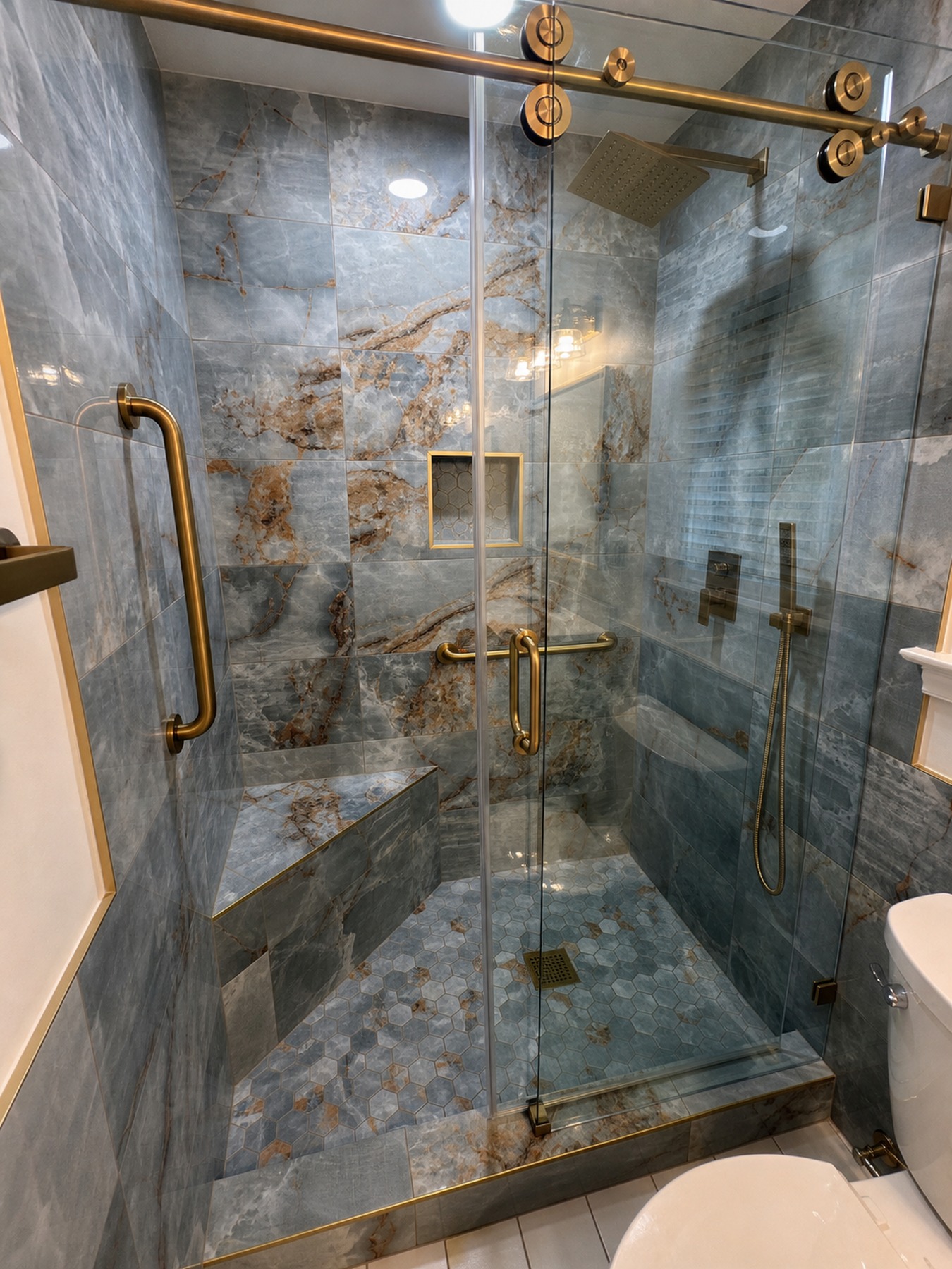 Luxury shower detail with glass enclosure, bench, and gold fixtures
