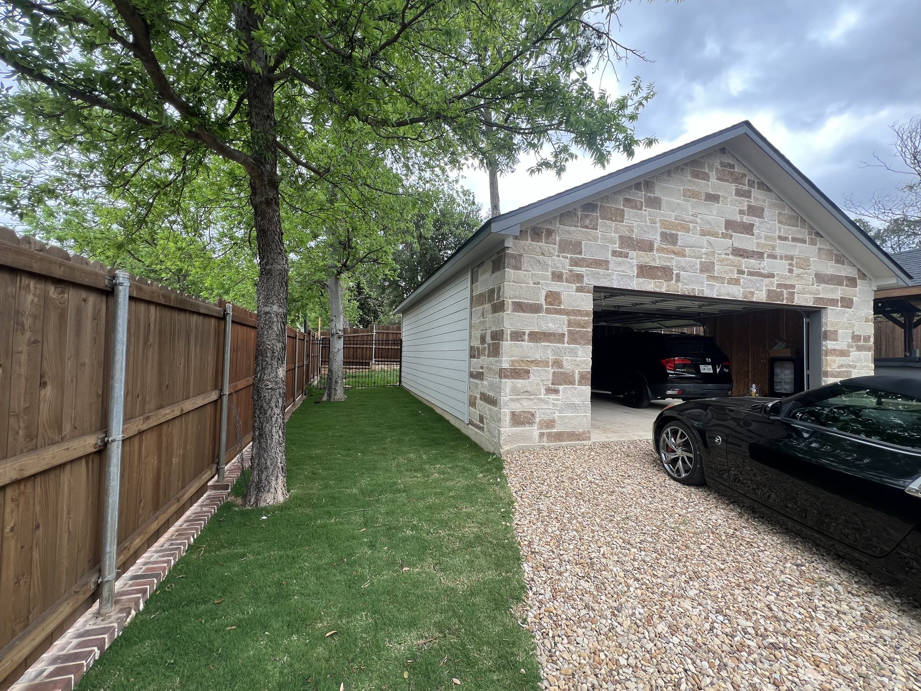 Finished side yard with gravel drive, lawn, and stone garage exterior