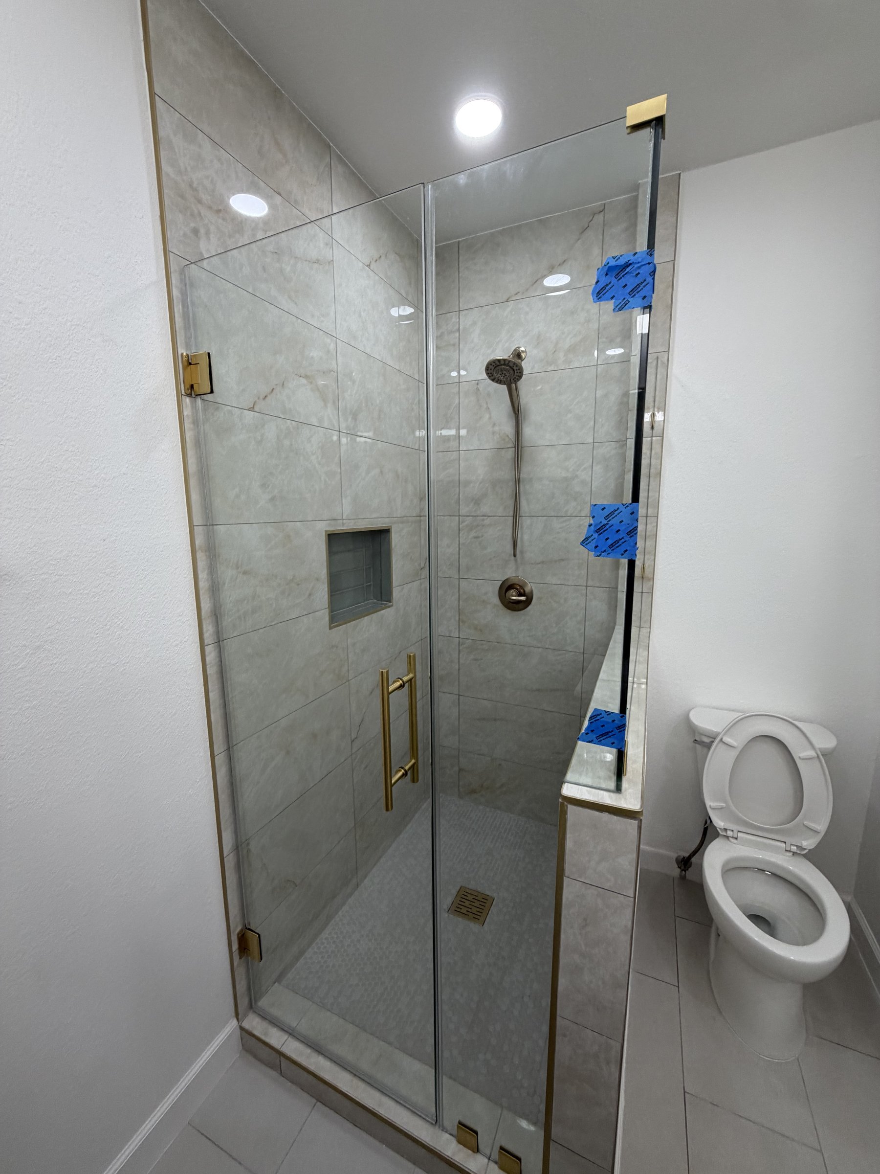 New walk-in shower with marble-look tile, brass controls, and glass enclosure