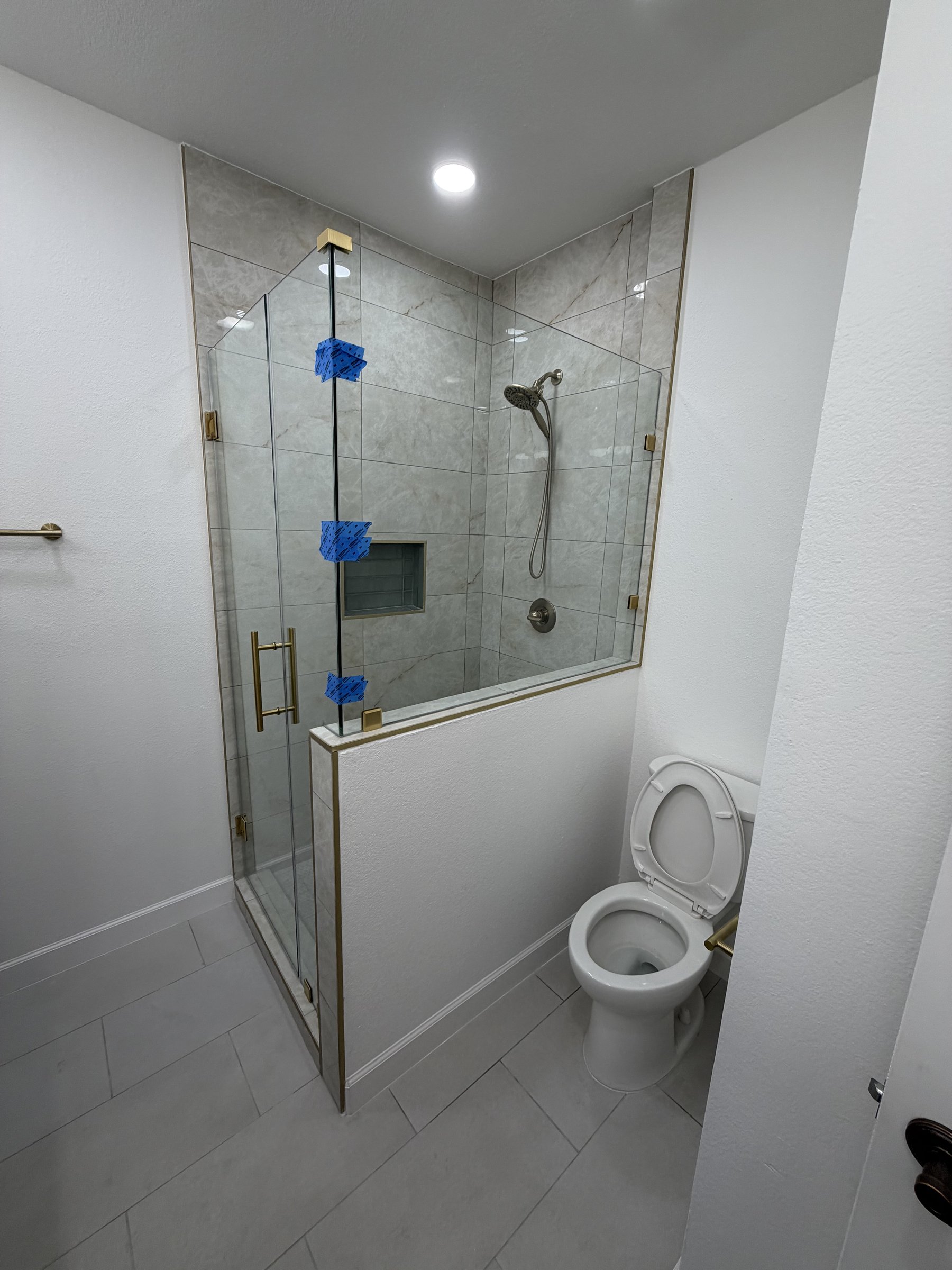 New walk-in glass shower with marble-look tile, brass trim, and modern toilet