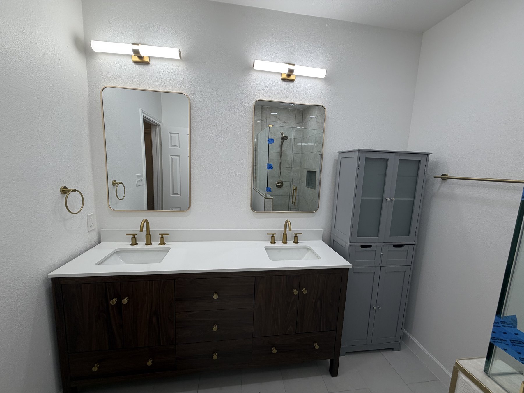 Modern master bathroom with dark wood double-vanity, brass fixtures, and walk-in shower view