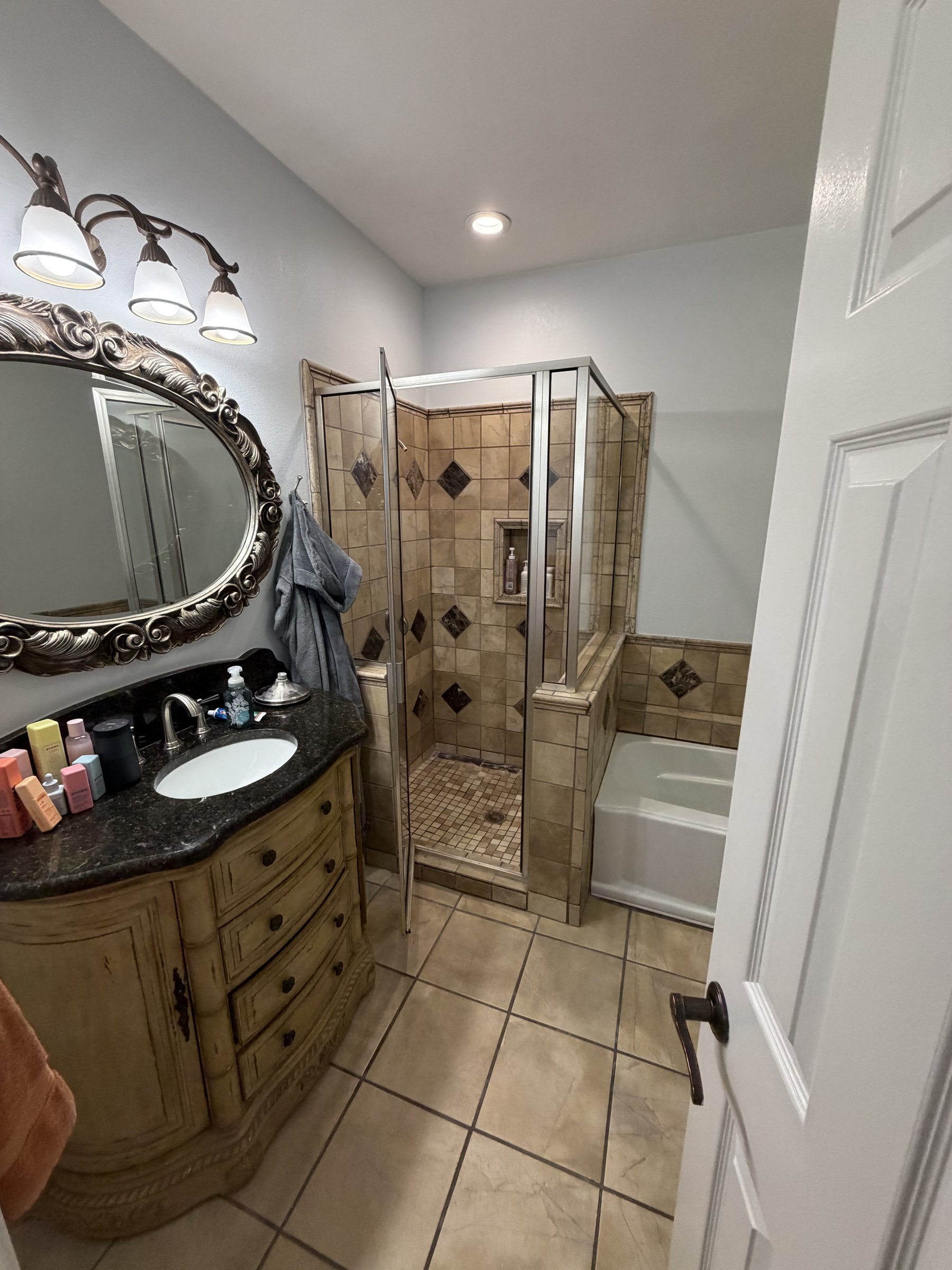 Dated master bathroom with cream tile, beige ornate vanity, and gold mirror — before renovation