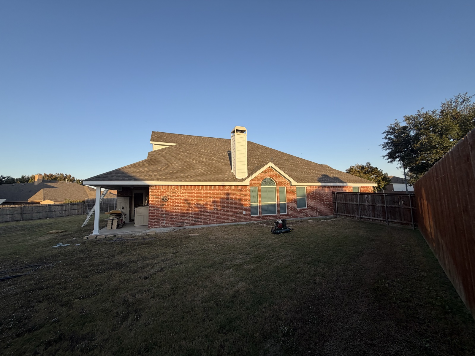 Finished residential roof replacement on a brick home, side elevation at golden hour
