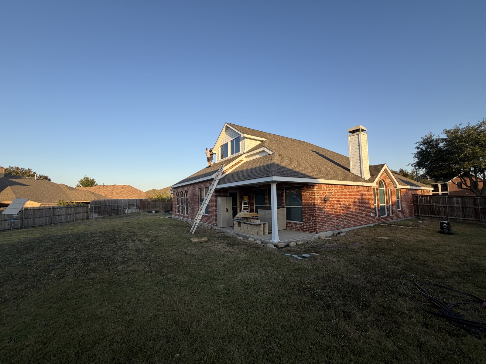 Crew working on the rear elevation of a brick home during a roof replacement